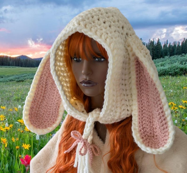 May include: A white crocheted hooded scarf with pink bunny ears. The scarf has a long tie that can be tied in a bow.