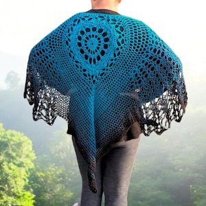 May include: A blue and black crochet shawl with a circular design in the center. The shawl has a gradient effect, transitioning from blue to black at the edges. The open weave creates a delicate, lacy appearance. The shawl is worn over a black top.