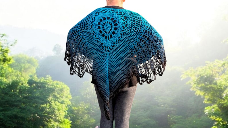May include: A blue and black crochet shawl with a circular design in the center. The shawl has a gradient effect, transitioning from blue to black at the edges. The open weave creates a delicate, lacy appearance. The shawl is worn over a black top.