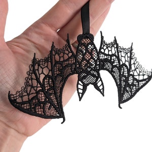 May include: Black lace bat ornament with intricate details. The bat is hanging from a black ribbon.