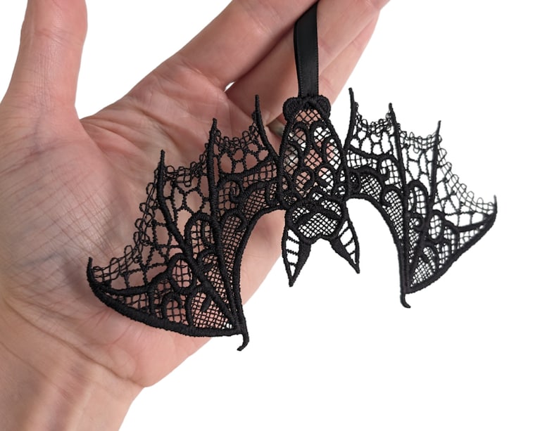 May include: Black lace bat ornament with intricate details. The bat is hanging from a black ribbon.