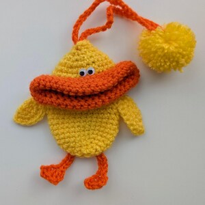 May include: A handmade yellow crochet duck ornament with an orange beak, feet, and a loop for hanging. The duck has googly eyes and a yellow pom-pom attached. This whimsical decoration is perfect for a nursery or children's room.
