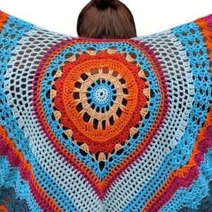 May include: A colorful, handmade crochet shawl with a central circular design. The shawl features a vibrant palette of blue, orange, pink, and white, creating a striking visual pattern. The open weave adds a delicate texture to the garment.