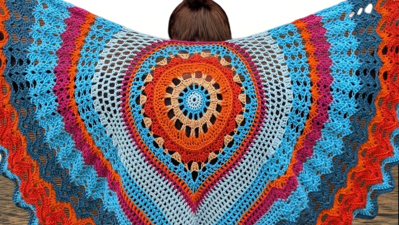 May include: A colorful, handmade crochet shawl with a central circular design. The shawl features a vibrant palette of blue, orange, pink, and white, creating a striking visual pattern. The open weave adds a delicate texture to the garment.