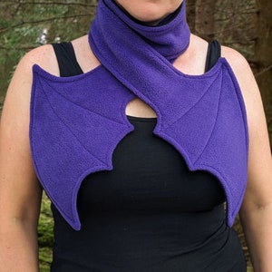 May include: Purple fleece scarf with bat wings attached. The scarf is worn around the neck and the wings drape over the shoulders.