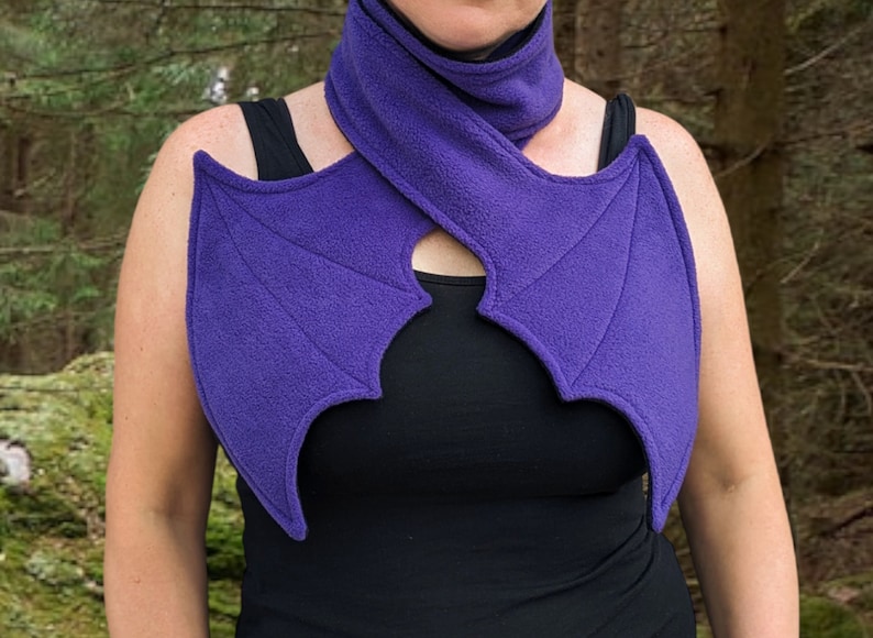 May include: Purple fleece scarf with bat wings attached. The scarf is worn around the neck and the wings drape over the shoulders.