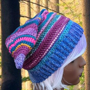Może przedstawiać: Kolorowa, ręcznie robiona czapka typu beanie w odcieniach niebieskiego, fioletowego, r&oacute;żowego i turkusowego. Czapka ma prążkowany wz&oacute;r i luźny kr&oacute;j, idealna do dodania odrobiny koloru do każdego stroju. Czapka to przytulny i stylowy dodatek.
