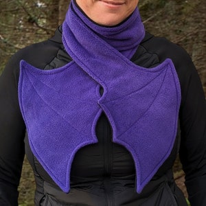 May include: Purple fleece scarf with bat wings attached. The scarf is worn around the neck and the wings extend out from the shoulders.