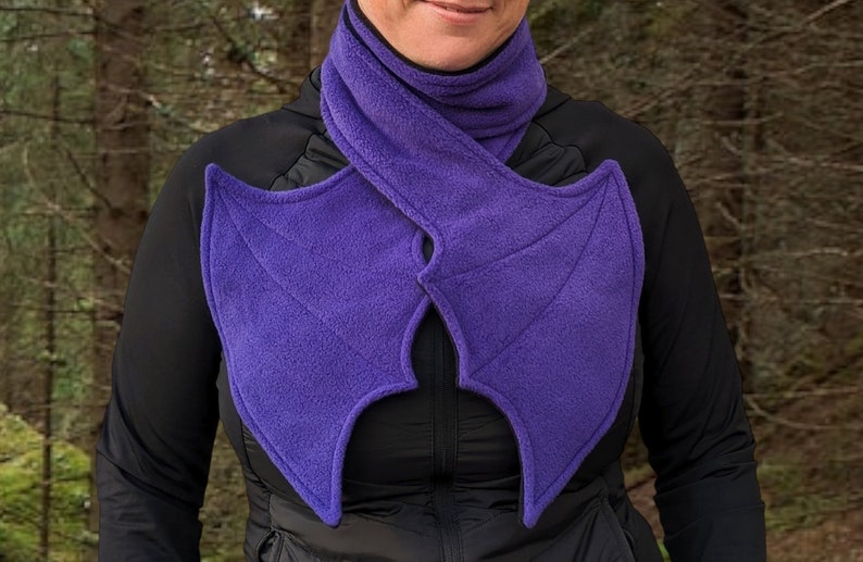 May include: Purple fleece scarf with bat wings attached. The scarf is worn around the neck and the wings extend out from the shoulders.