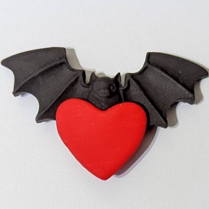 May include: A black bat with outstretched wings holding a red heart in its claws.