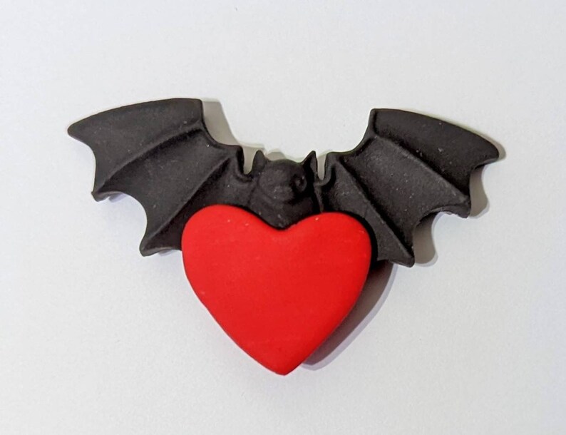 May include: A black bat with outstretched wings holding a red heart in its claws.