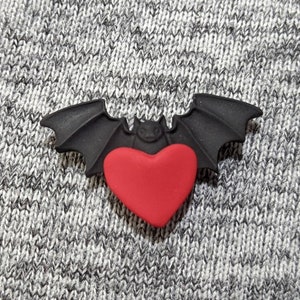 May include: A black bat with outstretched wings holding a red heart in its claws.