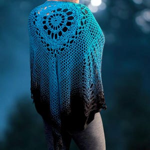 May include: A blue and black crochet shawl with a circular design on the back. The shawl is a gradient of blue to black. The shawl is worn over a person's shoulders.