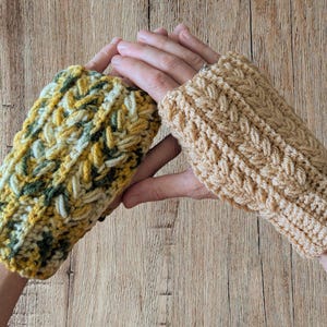 May include: Two handmade crochet fingerless gloves. One glove is a mix of yellow, green, and white yarn, while the other is a solid tan color. Both gloves have a textured, braided design.