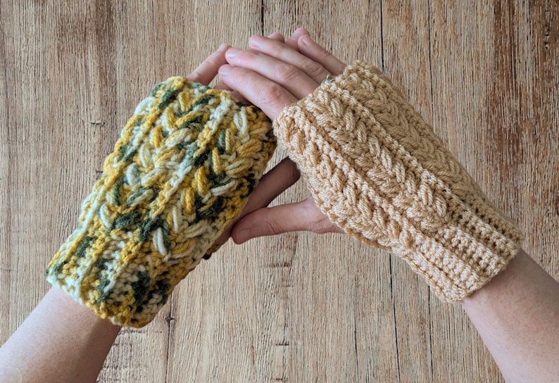 May include: Two handmade crochet fingerless gloves. One glove is a mix of yellow, green, and white yarn, while the other is a solid tan color. Both gloves have a textured, braided design.