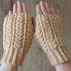 May include: A pair of beige fingerless gloves with a textured, woven pattern. The gloves are made of a soft yarn and have a ribbed cuff. The design features a repeating leaf-like motif.