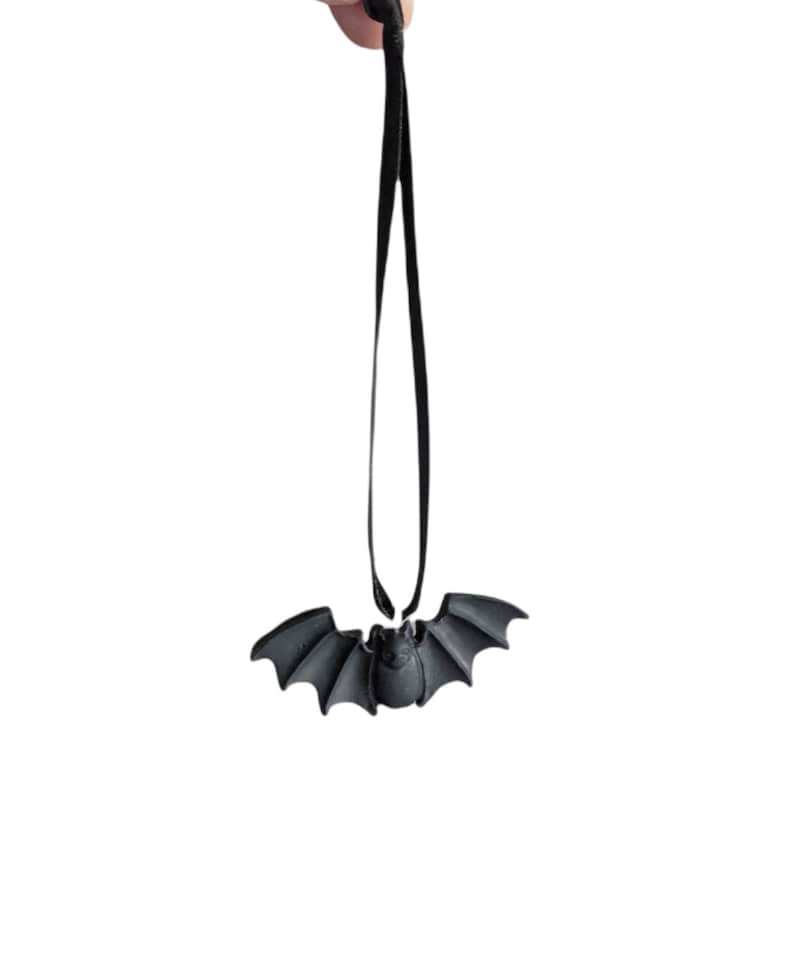Puede incluir: Un amuleto negro en forma de murci&eacute;lago cuelga de una cuerda negra. El amuleto es una decoraci&oacute;n de Halloween.