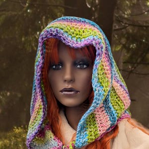 May include: A colourful crocheted hooded scarf with a rainbow pattern. The scarf is tied at the neck with long tassels.