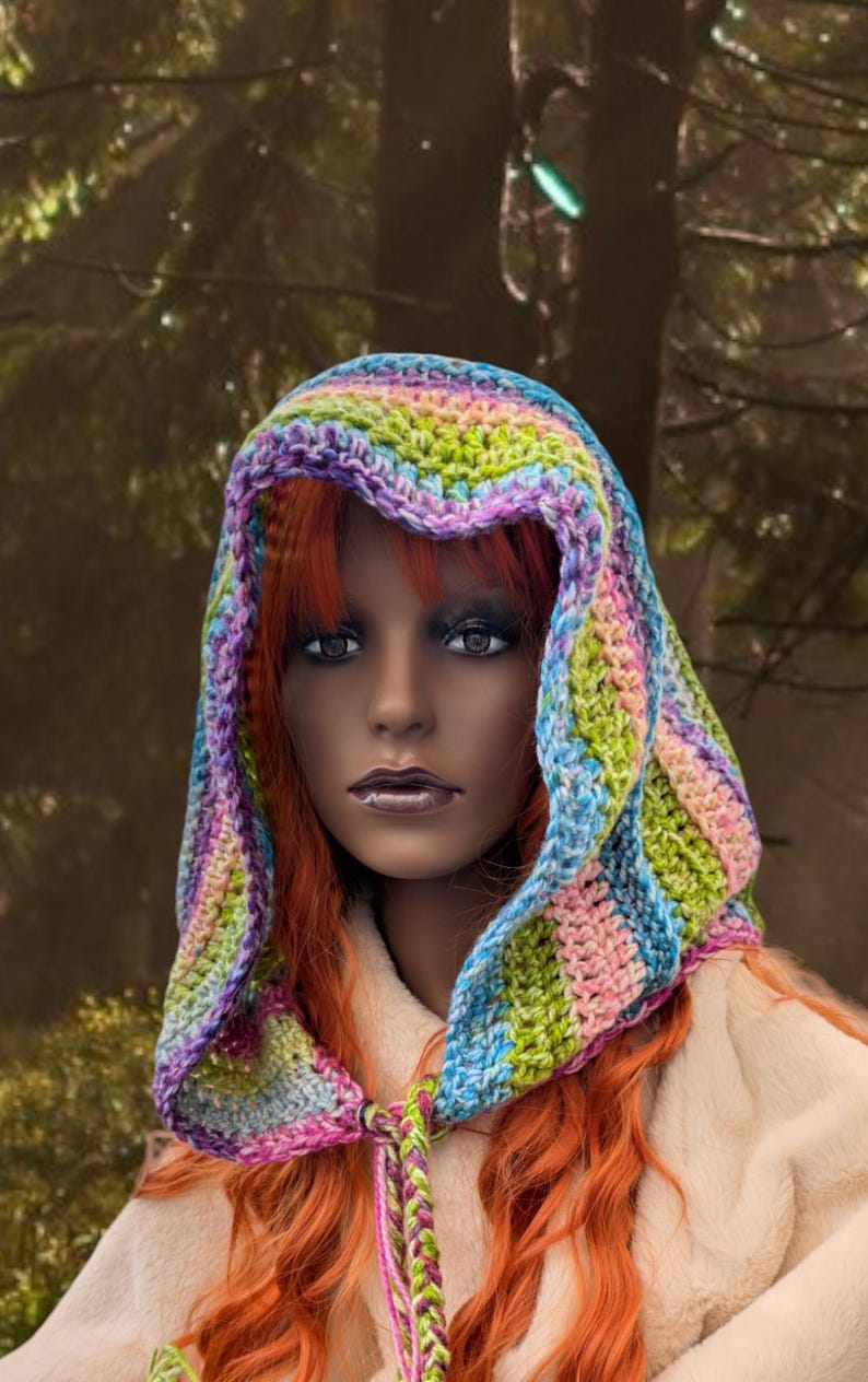 May include: A colourful crocheted hooded scarf with a rainbow pattern. The scarf is tied at the neck with long tassels.