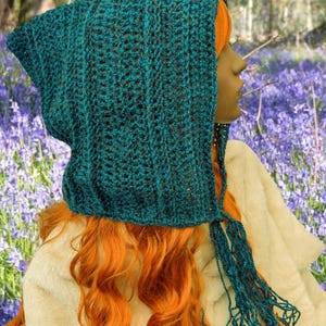 May include: A teal blue crochet hooded scarf with a long fringe. The scarf is made with a textured stitch and has a pointed hood.