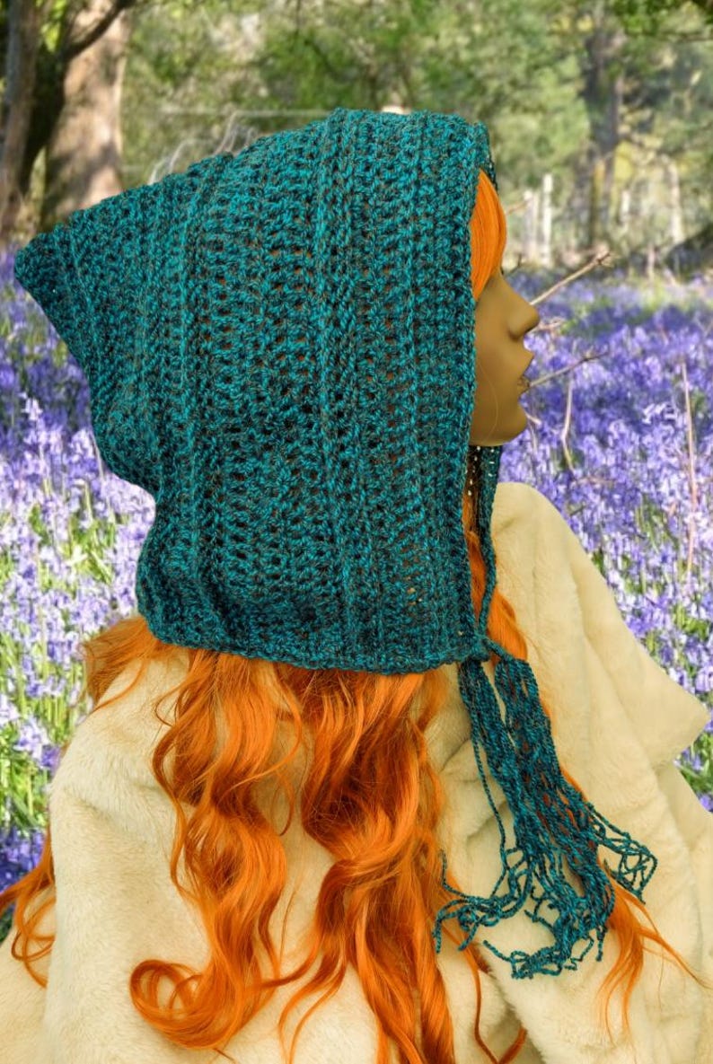 May include: A teal blue crochet hooded scarf with a long fringe. The scarf is made with a textured stitch and has a pointed hood.