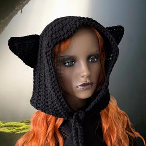Puede incluir: Sombrero de punto negro con capucha y orejas de gato. La capucha est&aacute; atada al cuello con un cord&oacute;n largo y delgado.