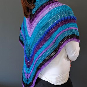 May include: A handmade crochet shawl in shades of teal, purple, and black. The shawl features a V-neck design and is adorned with textured bobbles along the edge. The color scheme creates a striking visual appeal.