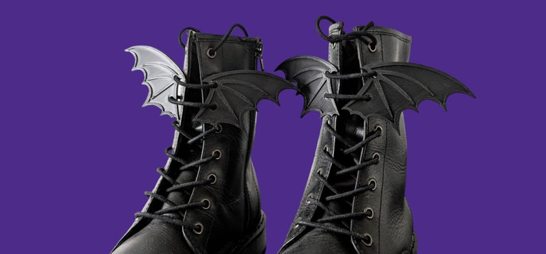 May include: A pair of black leather boots with bat wing lace charms. The charms are silver and black.