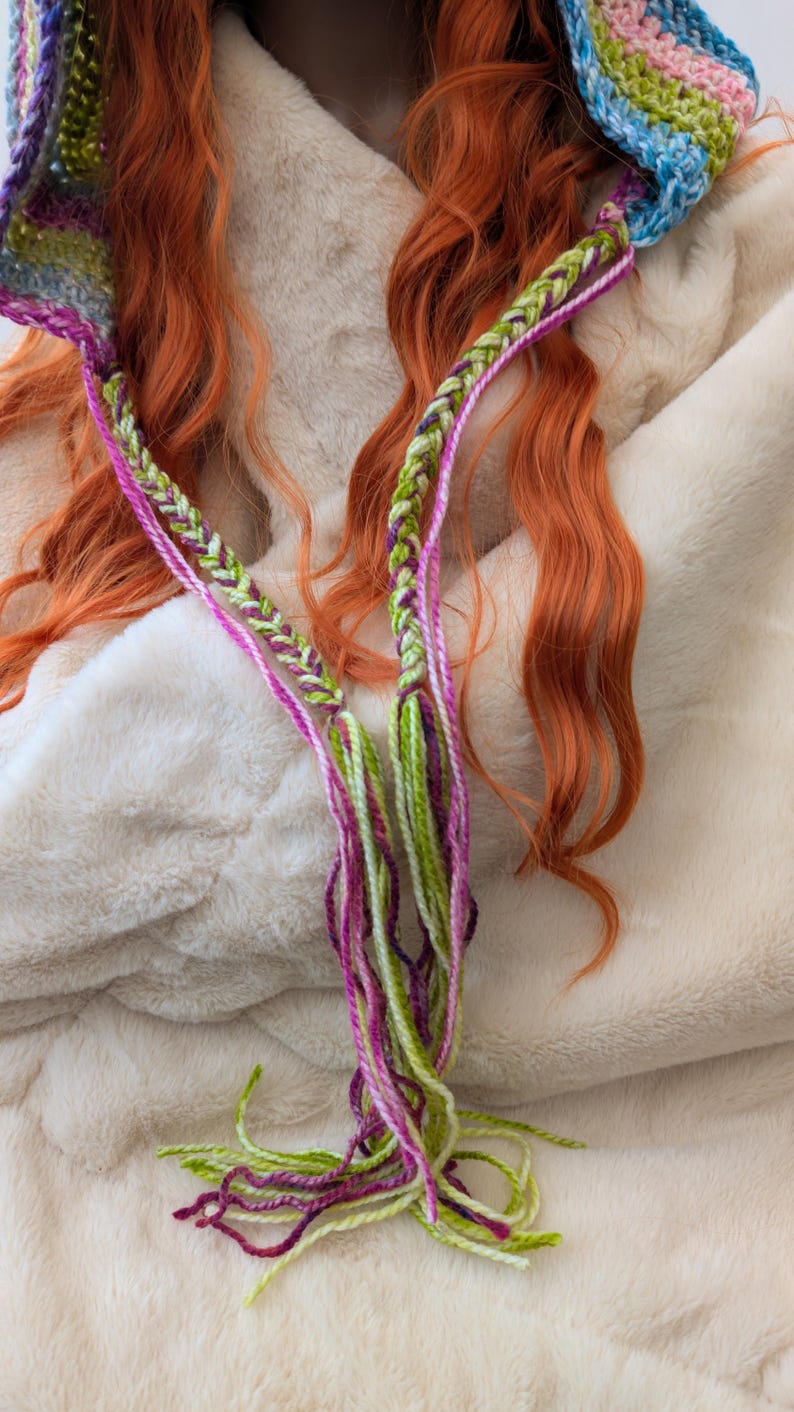 May include: A crocheted hat with long, colourful tassels. The hat is made with a variety of colours, including pink, green, blue, and purple. The tassels are made with the same colours of yarn as the hat.