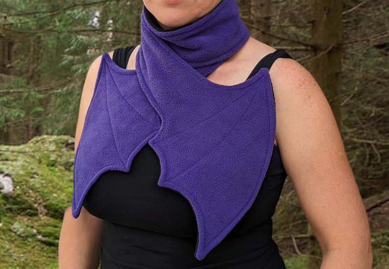 May include: Purple fleece scarf with bat wings. The scarf is worn around the neck and the wings drape over the shoulders.
