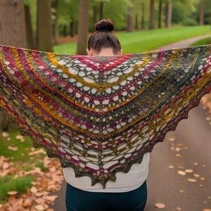 May include: A colorful, handmade shawl with a triangular shape. The shawl features a complex openwork design in shades of green, red, yellow, and brown. The shawl is held up, showcasing its intricate pattern and autumnal color palette.