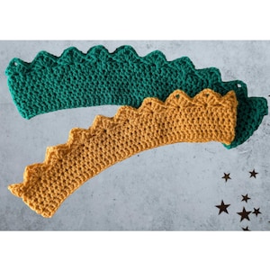 Puede incluir: Dos diademas de ganchillo con borde festoneado. Una es de color verde vibrante y la otra de color amarillo mostaza cálido. Las diademas están hechas a mano y parecen suaves y cómodas. El fondo es una superficie gris claro con confeti en forma de estrella.