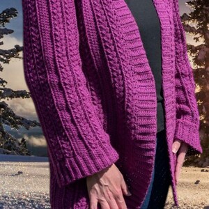 May include: A vibrant purple, open-front cardigan with a cable knit design. The long-sleeved sweater features a ribbed texture and a relaxed fit. The cardigan is made of a soft, warm material, perfect for layering during cooler weather.