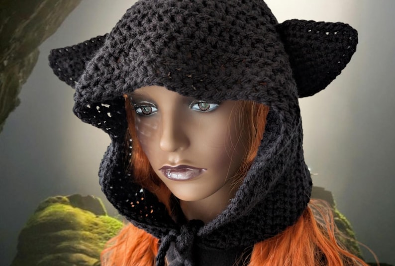 Puede incluir: Un gorro de punto negro con capucha y orejas de gato. El gorro est&aacute; hecho con un delicado patr&oacute;n de punto abierto y tiene una capucha larga y fluida.