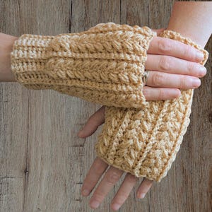 May include: A pair of light tan crochet fingerless gloves. The gloves feature a textured cable knit design. The wrist cuffs are ribbed, and the gloves cover the hand up to the knuckles, leaving the fingers free.