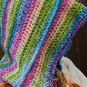 May include: A colourful crocheted hooded scarf with a rainbow striped pattern. The scarf is made with a variety of colours, including pink, blue, green, and purple.