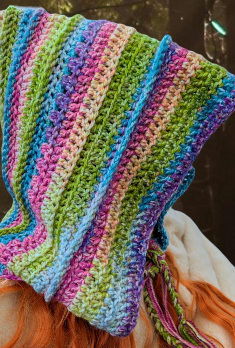 May include: A colourful crocheted hooded scarf with a rainbow striped pattern. The scarf is made with a variety of colours, including pink, blue, green, and purple.