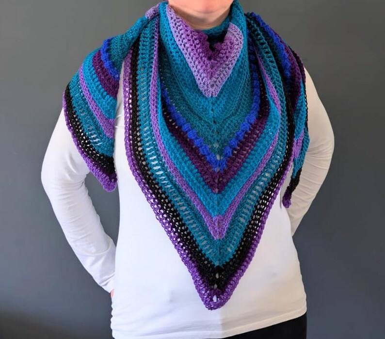 Pu&ograve; includere: Uno scialle triangolare all'uncinetto fatto a mano. Lo scialle presenta una sfumatura di colori turchese, viola, blu e nero. Il motivo all'uncinetto crea un design strutturato e aperto. Un accessorio fatto a mano che aggiunge fascino a qualsiasi outfit.