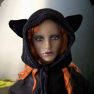 May include: Black crocheted hooded hat with cat ears. The hat has a long tie that can be tied under the chin.