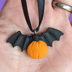 May include: A black bat charm with an orange pumpkin hanging from a black ribbon. Halloween themed ornament.