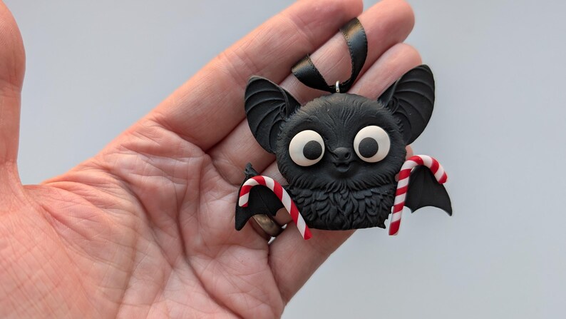 Puede incluir: Adorno de murci&eacute;lago negro con grandes ojos blancos y alas de bast&oacute;n de caramelo. El murci&eacute;lago tiene un pecho peludo y orejas grandes. Se adjunta una cinta negra para colgar. Ideal para Halloween o Navidad.
