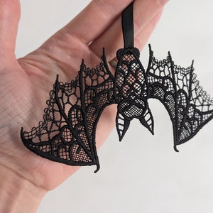 May include: Black lace bat ornament with a delicate design. The bat is hanging from a black ribbon.