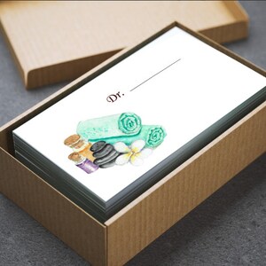 May include: A stack of white cards inside a brown box. The cards feature a watercolor illustration of spa elements, including rolled green towels, black stones, and essential oil bottles. The word "Dr." is printed at the top.