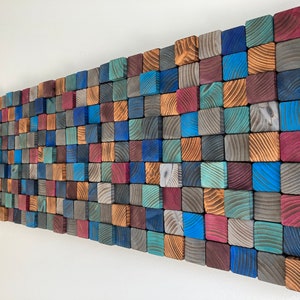 May include: A wall art piece made of wooden squares in various shades of blue, brown, red, and gray. The squares are arranged in a staggered pattern to create a textured and modern look.