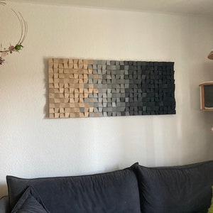 Peut inclure: Une œuvre d'art murale rectangulaire en bois avec un motif dégradé. L'œuvre passe du beige clair au gris, puis au noir. L'œuvre est fixée sur un mur blanc au-dessus d'un canapé gris foncé.