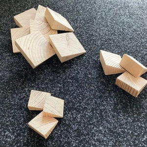 May include: A collection of small, unfinished wooden blocks. The blocks are square with one corner cut off, revealing the wood grain. They are scattered on a dark gray textured surface.