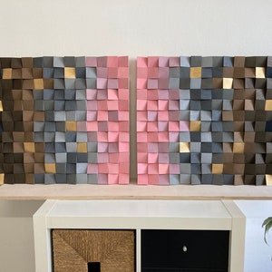May include: A wall art piece made of wood blocks in shades of brown, gray, black, pink and gold. The blocks are arranged in a geometric pattern, creating a modern and abstract design.