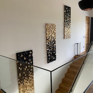 Puede incluir: Tres piezas de arte de pared geométricas en negro y dorado cuelgan de una pared blanca en una casa moderna. Las piezas de arte están hechas de madera y tienen un diseño degradado.