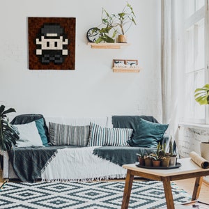 May include: A living room interior with a couch, a coffee table, and a plant. A pixel art picture of a person wearing a hat is hanging on the wall.
