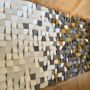 May include: A large, rectangular wooden wall art piece. The artwork is composed of numerous small, angled wooden blocks in shades of white, gray, brown, and yellow. The blocks create a textured, three-dimensional effect, suitable for home decor.